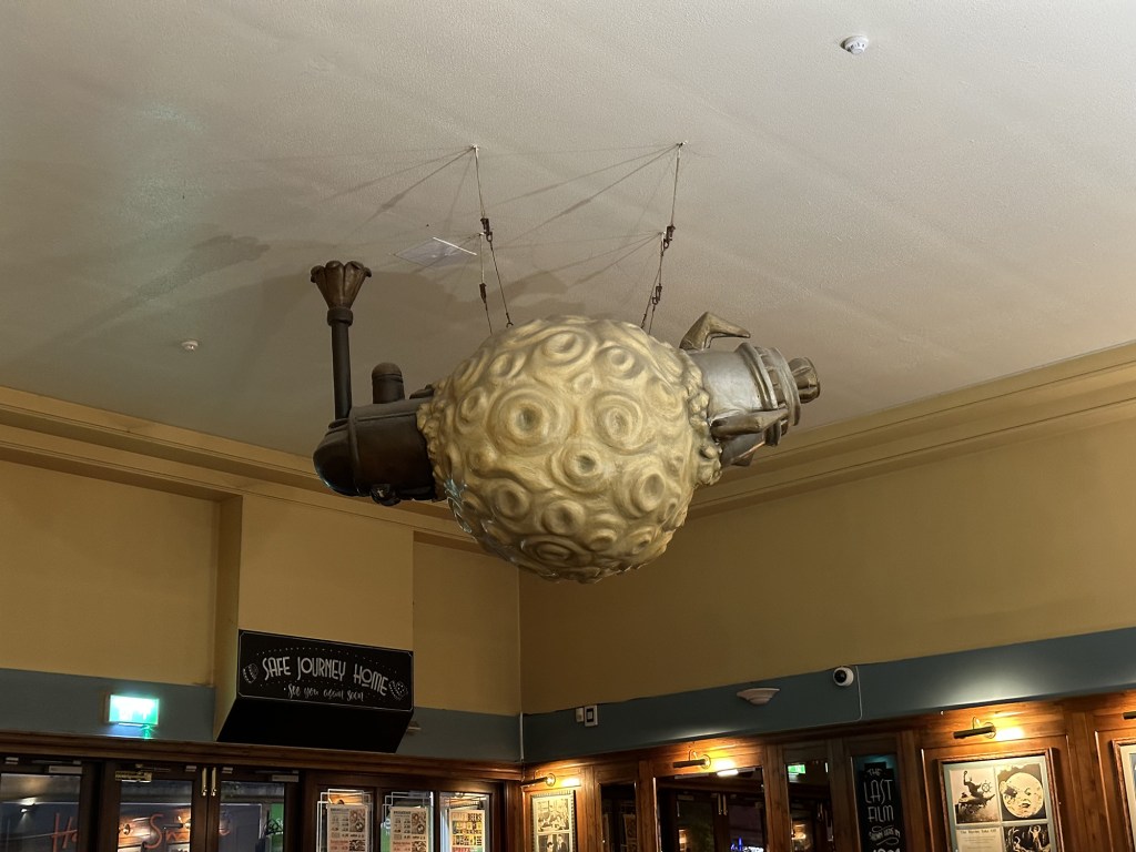 This Wetherspoon contains a peculiar sculpture, likely a reference to an old film. A large ball, seemingly the moon, has been blasted through by a rocket and a train.